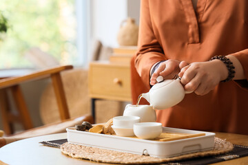 Asian woman pouring tea on table at home, closeup