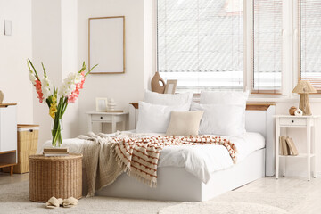 Comfortable bed, wicker table and vase with beautiful gladiolus flowers in interior of bedroom