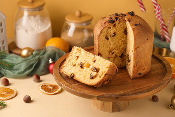 Wooden stand with cut Panettone and Christmas decor on beige background