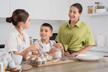 Young mother with her children preparing dough in kitchen