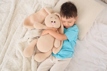 Sleeping little boy hugging toy bunny on bed, top view