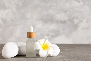 Bottle of essential oil, tropical flower and spa stones on grunge background