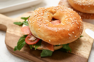 Wooden board of tasty bagel sandwich with salmon fish and arugula on white background, closeup