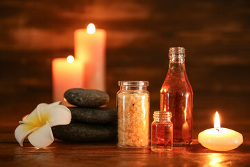 Spa composition with plumeria flower, stones and burning candles on dark wooden table, closeup