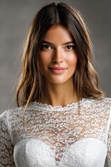 A smiling young woman in a delicate lace bridal dress showcases elegant natural makeup, exuding confidence and warmth against a soft gray studio background.