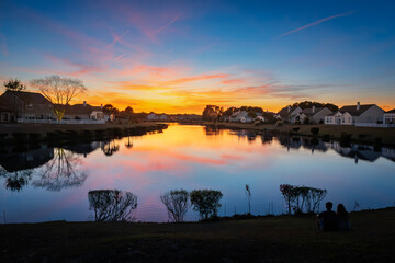 Fototapeta premium A young couple sits on the banks of a lake under a colorful sunset at a residential community in Conway, South Carolina.