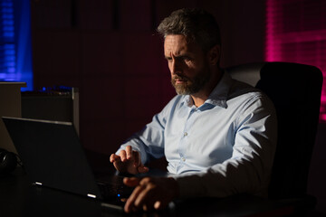 Business man using laptop late at night office. Overworked businessman at a desk with a hard office work. Business man on office night background. Worker bored and tired in dark office.