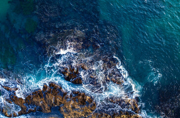 Summer rocky beach. Coastline from above. Surf hitting rocks. Clear turquoise water coastline. Crashing waves aerial. Summer beach with crashing waves. Ocean water texture. Tropical coastline.