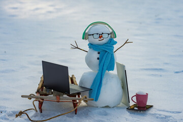 Winter online shopping. Creative winter snowman with computer setup. Remote online work winter concept. Snowman using laptop outside. Winter snowman typing on laptop in snow.