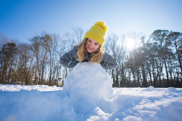 Happy winter. Child in warm winter clothes play with snow. Kid rolling snowball on winter morning....