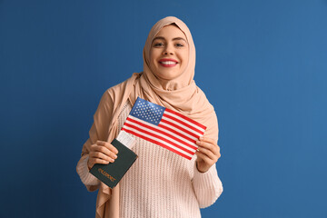 Beautiful young happy Muslim woman with USA flag, passport and ticket on blue background