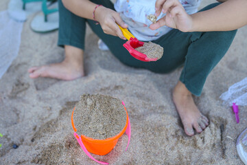 A faceless photo showing a small child playing in the sand using colorful tools.