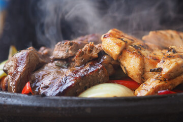 Juicy meats cooking on grill with vegetables in background