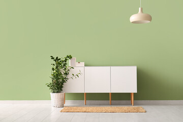 Modern chest of drawers with houseplant and lamp near green wall in room