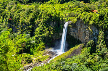 Manto de la Novia waterfall flows into Pastaza river in Banos, Ecuador. Scenic landscape features white water and tourist cable car in lush green canyon