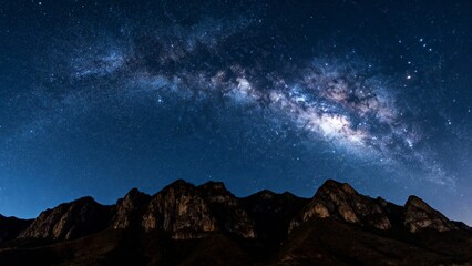 Fototapeta premium Milky Way galaxy arching over rugged mountain peaks under a star-filled night sky