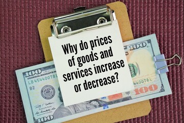 Paper money and a whiteboard with the words of a question about economics, namely Why do prices of goods and services increase or decrease?