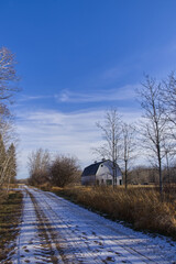 Snow on a dirt road with a Barn at the side