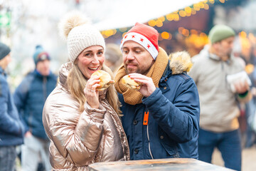 Happy couple enjoying sausages and fresh rolls at a bright Christmas market sharing warm holiday flavors