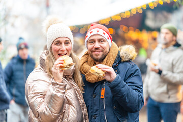 Cheerful couple eating sausages and rolls at a festive Christmas market enjoying warm winter flavors together