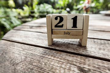 Wooden cube calendar for 21st July place on a table in a sunny garden background