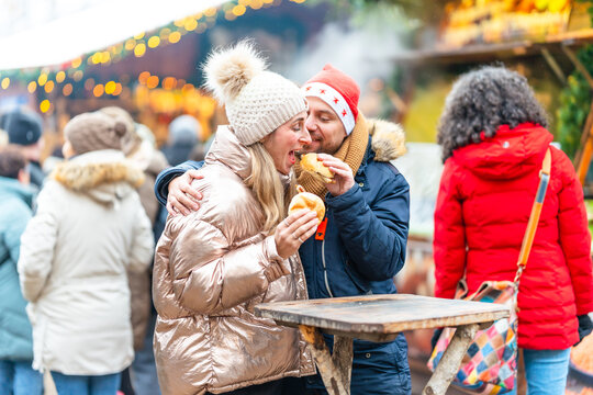 Joyful couple enjoying sausages and rolls at a lively Christmas market sharing tasty winter holiday moments