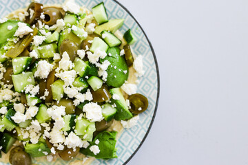 healthy nourish bowl with avocado, jalapeno, feta, green olives and cucumber on hummus