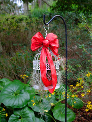 A white bird cage filled with garden clippings with a bright red bow hanging from a shepherd's hook