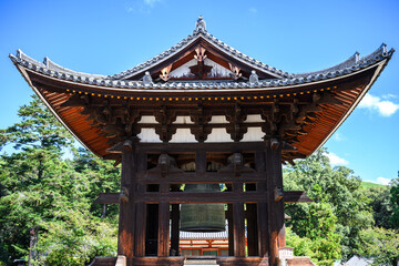 A majestic traditional wooden bell tower stands under a clear blue sky at a Buddhist temple complex.
