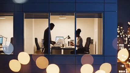 Exterior view of modern office building at night with colleagues working late behind glass windows. Concept of overtime, dedication and deadline. Perfect for corporate business themes.