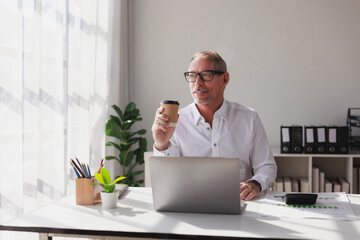 Mature businessman drinking coffee reflecting at office desk