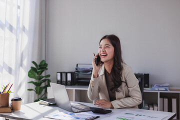 Asian businesswoman talking on phone and smiling at office desk
