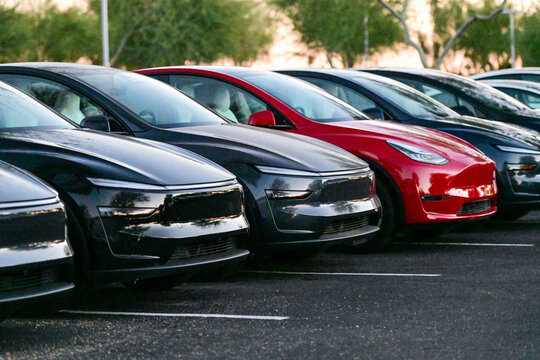 A row of Tesla vehicles parked in a lot, illustrating electric vehicle adoption, consumer transportation trends, and modern automotive technology