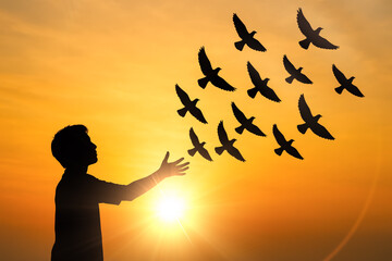 Silhouette of young man releasing flock of birds into vibrant orange sunset, a concept of hope, freedom and new beginnings
