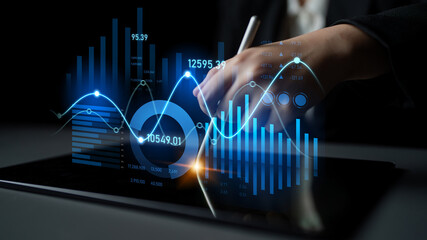 A close-up view of a hand using a pen to interact with digital graphs and charts on a tablet, showcasing professional business analytics in a modern office setting. Scalp