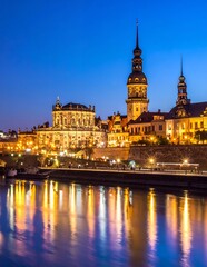 Obraz premium Dresden cityscape at night with illuminated buildings reflecting in the Elbe River, showcasing historic German architecture under a vibrant blue sky.