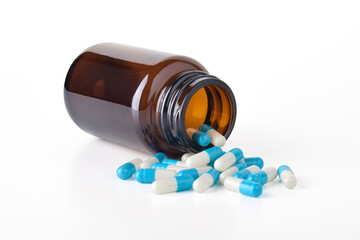 Antibiotic capsules spilling from a bottle on a white background. Blue and white capsule pills. Healthcare and pharmacy. Medical treatment pills. Pharmaceutical industry and medicine.