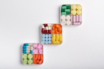 Various colorful pills and capsules in separate pill boxes on a white background, top view. Concept of medicine and health supplements.