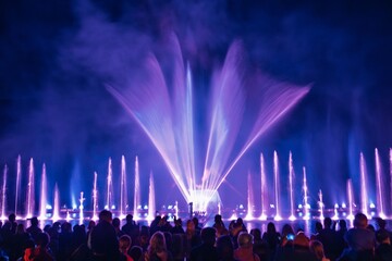 A stunning long exposure image of a nighttime water fountain show, featuring vibrant illuminated streams and a captivated crowd enjoying the spectacular display of water and light.