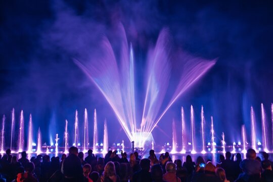A stunning long exposure image of a nighttime water fountain show, featuring vibrant illuminated streams and a captivated crowd enjoying the spectacular display of water and light. - Powered by Adobe