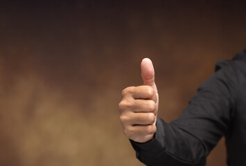 Hand showing thumbs up gesture on brown background.