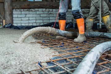 Construction workers pouring concrete over reinforcing mesh for a foundation. This image showcases construction and building projects. Ideal for articles, websites, and brochures.