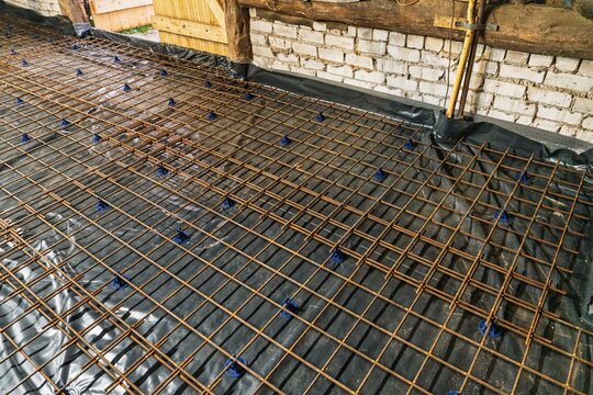 A construction site displays a reinforcement grid elevated by blue supports on a black membrane, prepared for a concrete slab pour, ensuring structural integrity and durability.
