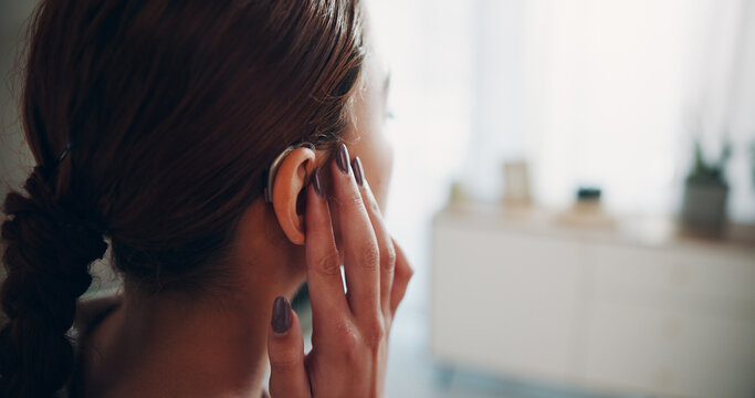 Hand, woman and touch hearing aid at house with ear device, testing sound and auditory assistance. Back, medical equipment and female person with disability, deaf and audio implant to improve speech