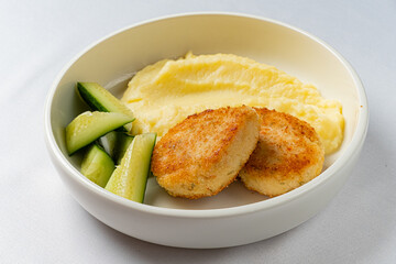 A warm bowl displays crispy chicken patties, smooth mashed potatoes, and fresh cucumber slices