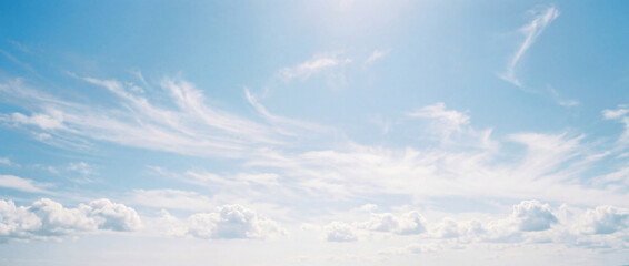 A wide panoramic view of a bright blue sky filled with soft white cumulus clouds and high wispy cirrus formations stretching across the horizon.