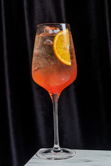 A vibrant cocktail in a tall glass, garnished with an orange slice, exudes summer vibes