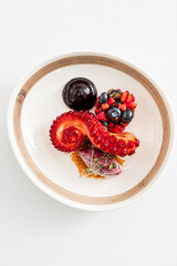 A beautifully presented seafood dish combines tender octopus with fresh fruits in artistic layers