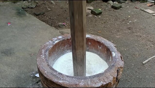 A traditional wooden mortar and pestle filled with white grains