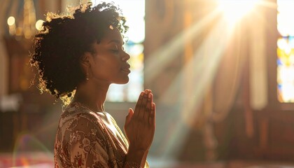 Young African American woman praying in church with sun rays.